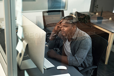 Buy stock photo Shot of a handsome young businessman sitting alone in the office and feeling stressed while using his computer