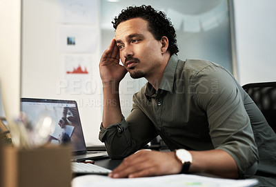 Buy stock photo Shot of a handsome young businessman sitting alone in the office and feeling stressed while using his computer