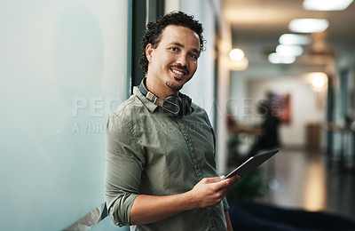 Buy stock photo Shot of a handsome young businessman standing in the office and using a digital tablet