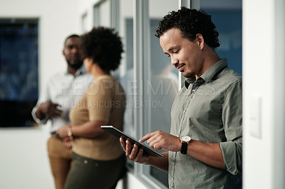 Buy stock photo Shot of a handsome young businessman standing in the office and using a digital tablet