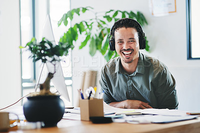 Buy stock photo Shot of a young businessman wearing headphones in an office