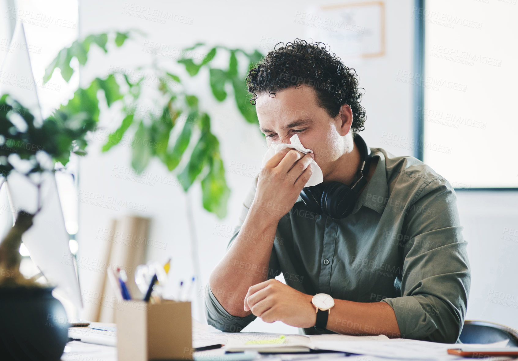 Buy stock photo Shot of a young businessman blowing his nose in an office