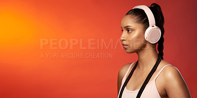 Buy stock photo Studio shot of a sporty young woman wearing headphones and posing with a skipping rope around her neck against a red background