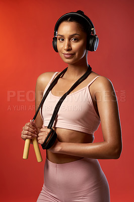Buy stock photo Studio portrait of a sporty young woman posing with a skipping rope around her neck against a red background