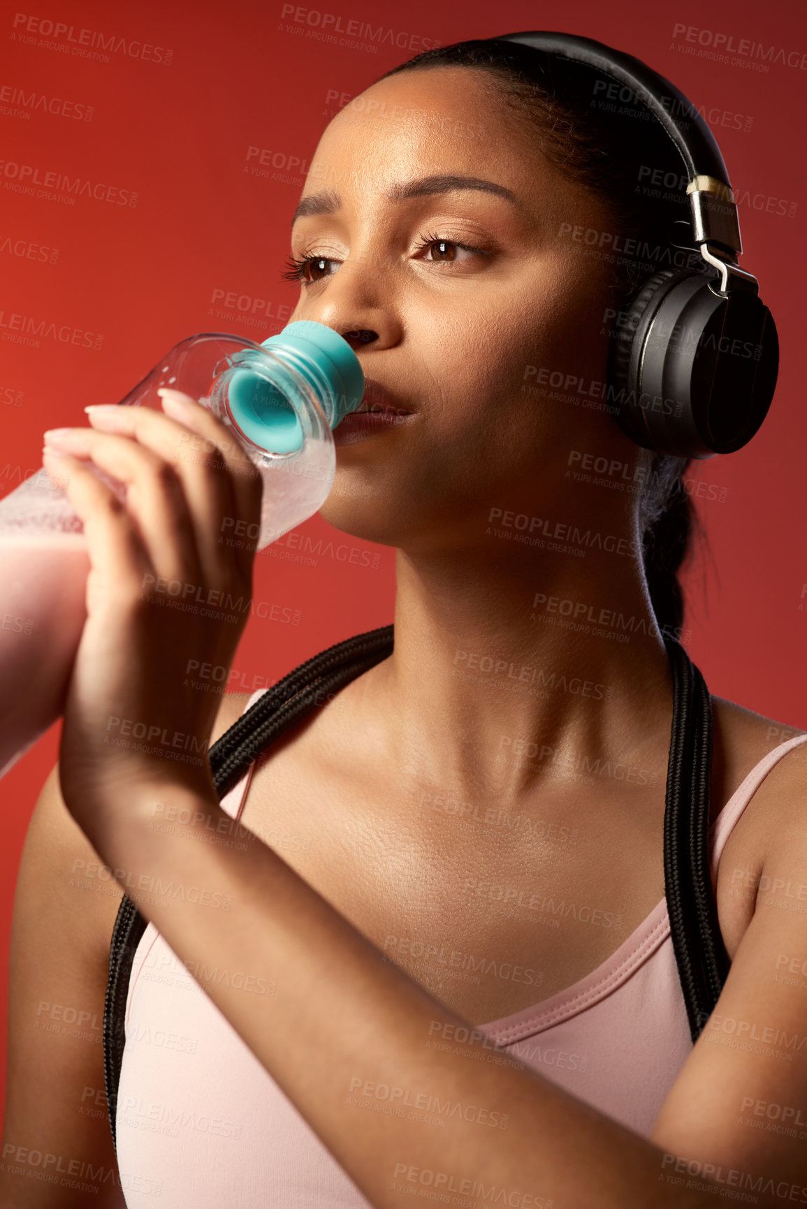 Buy stock photo Studio shot of a sporty young woman drinking water against a red background