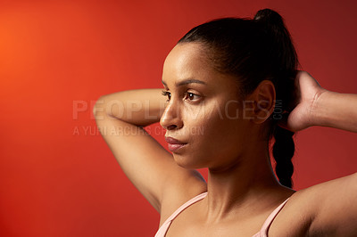 Buy stock photo Studio shot of a sporty young woman stretching her arms against a red background