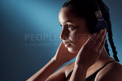 Buy stock photo Studio shot of a sporty young woman listening to music against a blue background