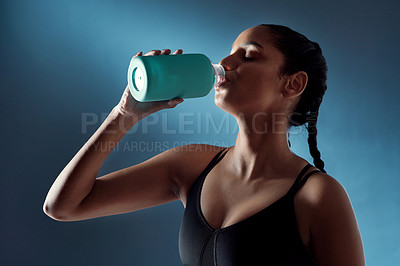 Buy stock photo Studio shot of a sporty young woman drinking water against a blue background