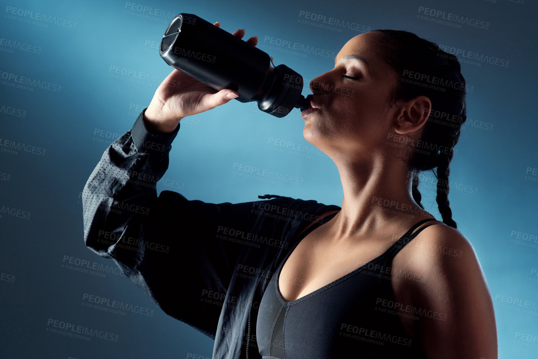 Buy stock photo Studio shot of a sporty young woman drinking water against a blue background