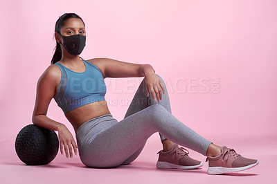 Buy stock photo Full length portrait of an attractive and sporty young woman wearing a mask and posing with a medicine ball in studio against a pink background