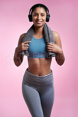 Buy stock photo Cropped portrait of an attractive and sporty young woman wearing headphones and posing with a towel in studio against a pink background