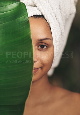 Buy stock photo Shot of a beautiful young woman wearing a towel around her head while posing behind a green leaf