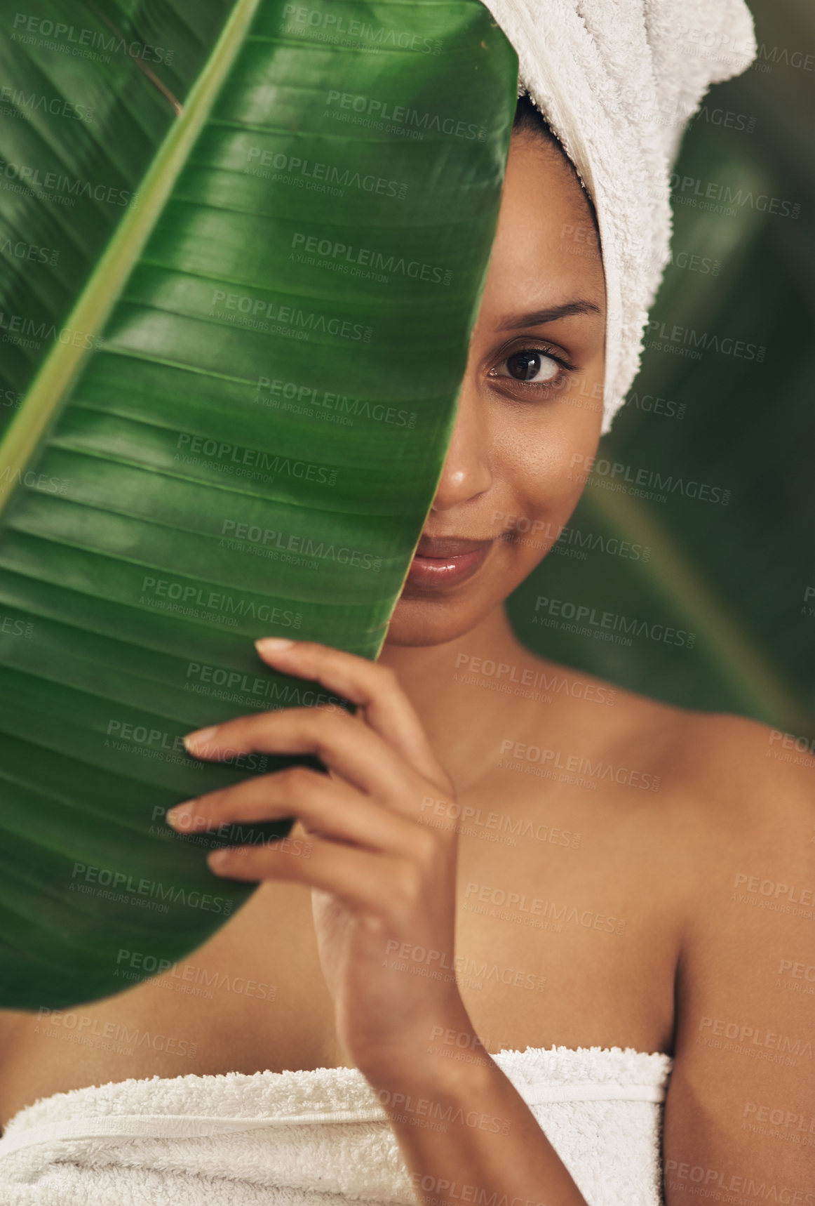 Buy stock photo Shot of a beautiful young woman wearing a towel around her head while posing behind a green leaf