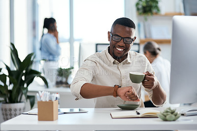 Buy stock photo Shot of a young businessman checking the time on his wristwatch while working in an office