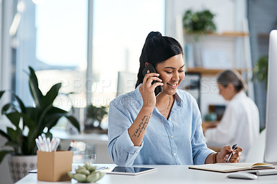 Buy stock photo Shot of a young businesswoman talking on a cellphone while going through notes in an office