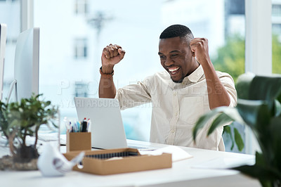 Buy stock photo Shot of a young businessman cheering while working on a laptop in an office