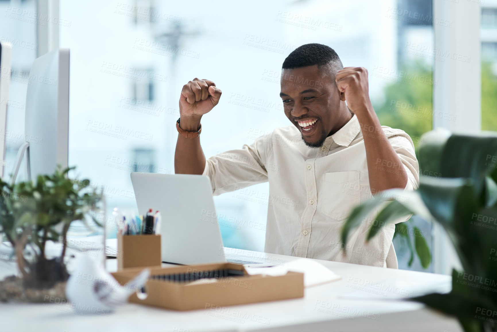 Buy stock photo Shot of a young businessman cheering while working on a laptop in an office