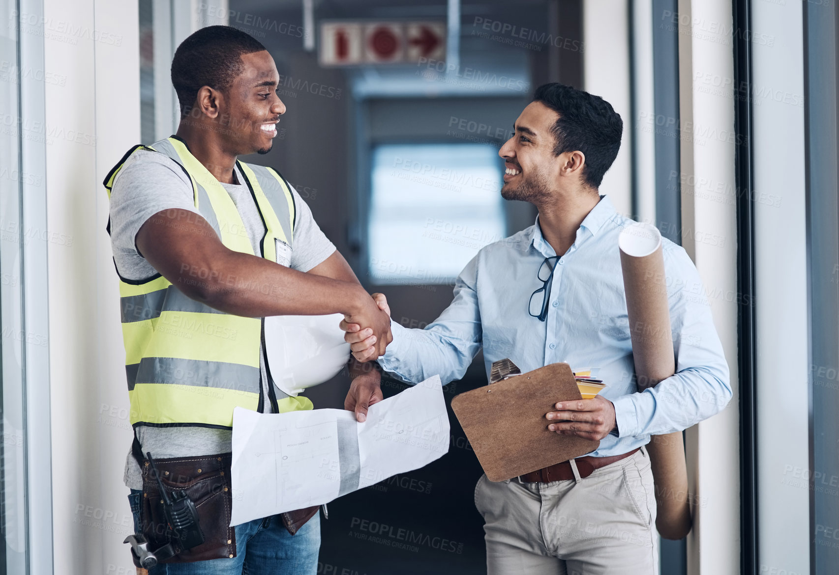 Buy stock photo Shot of two young architects standing together and shaking hands after a discussion about the room before they renovate