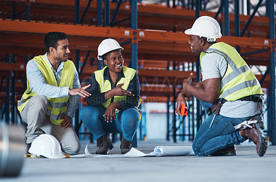 Buy stock photo Shot of a group of contractors crouching down in the warehouse together and using a blueprint to plan