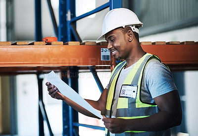 Buy stock photo Shot of a handsome young contractor standing in the warehouse and reading paperwork