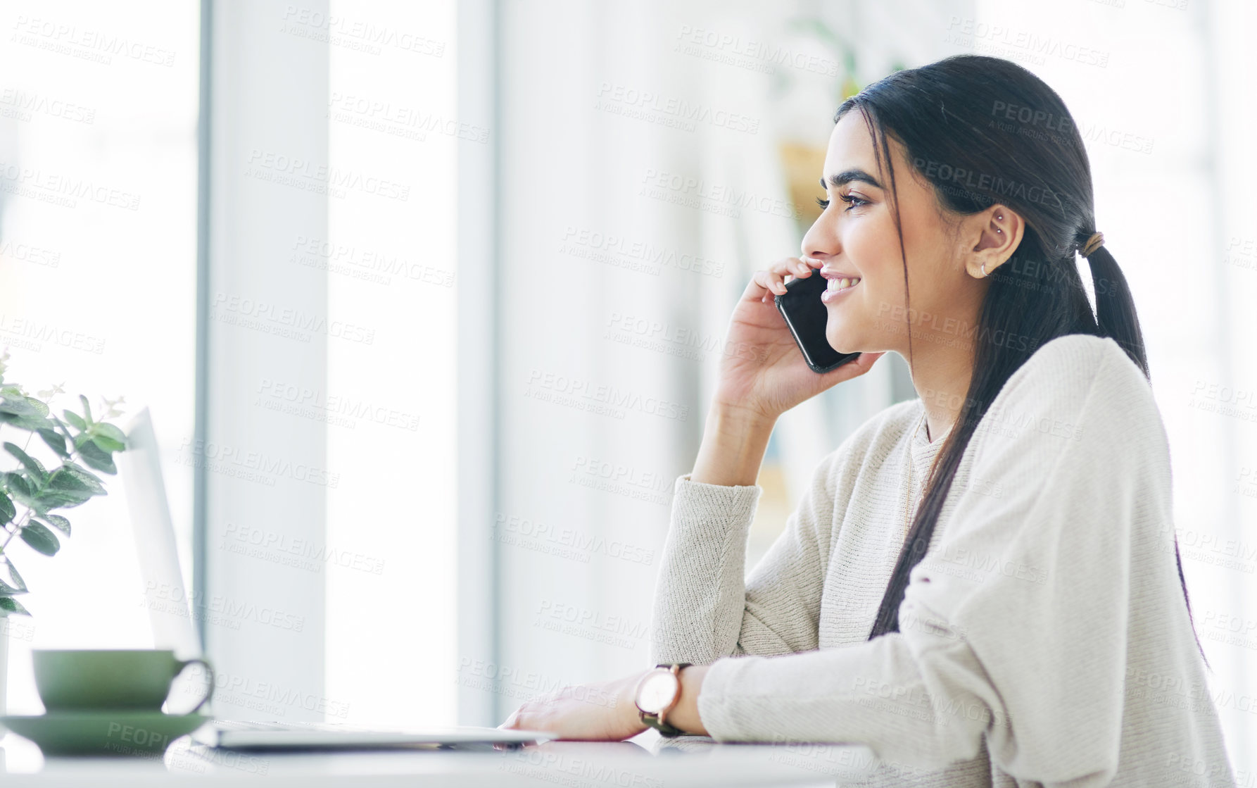 Buy stock photo Shot of a young businesswoman talking on a cellphone while using a laptop in an office