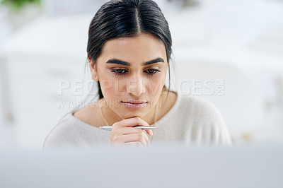 Buy stock photo High angle shot of a young businesswoman looking thoughtful while working on a computer in an office