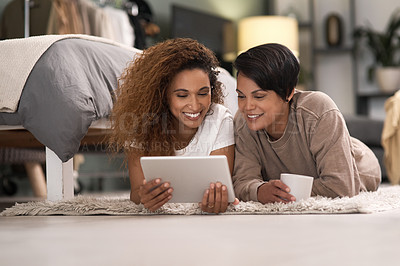 Buy stock photo Shot of a young lesbian couple using a tablet while relaxing in their bedroom