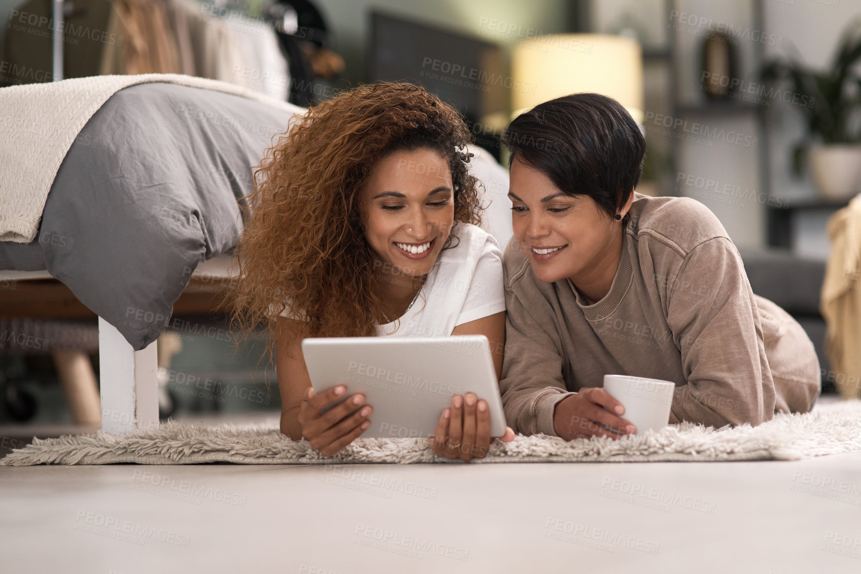 Buy stock photo Shot of a young lesbian couple using a tablet while relaxing in their bedroom