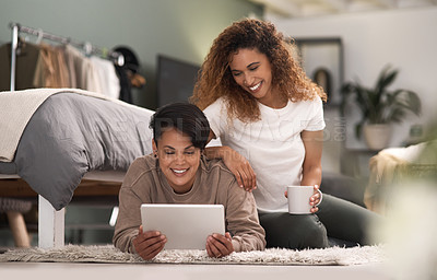 Buy stock photo Shot of a young lesbian couple using a tablet while relaxing in their bedroom