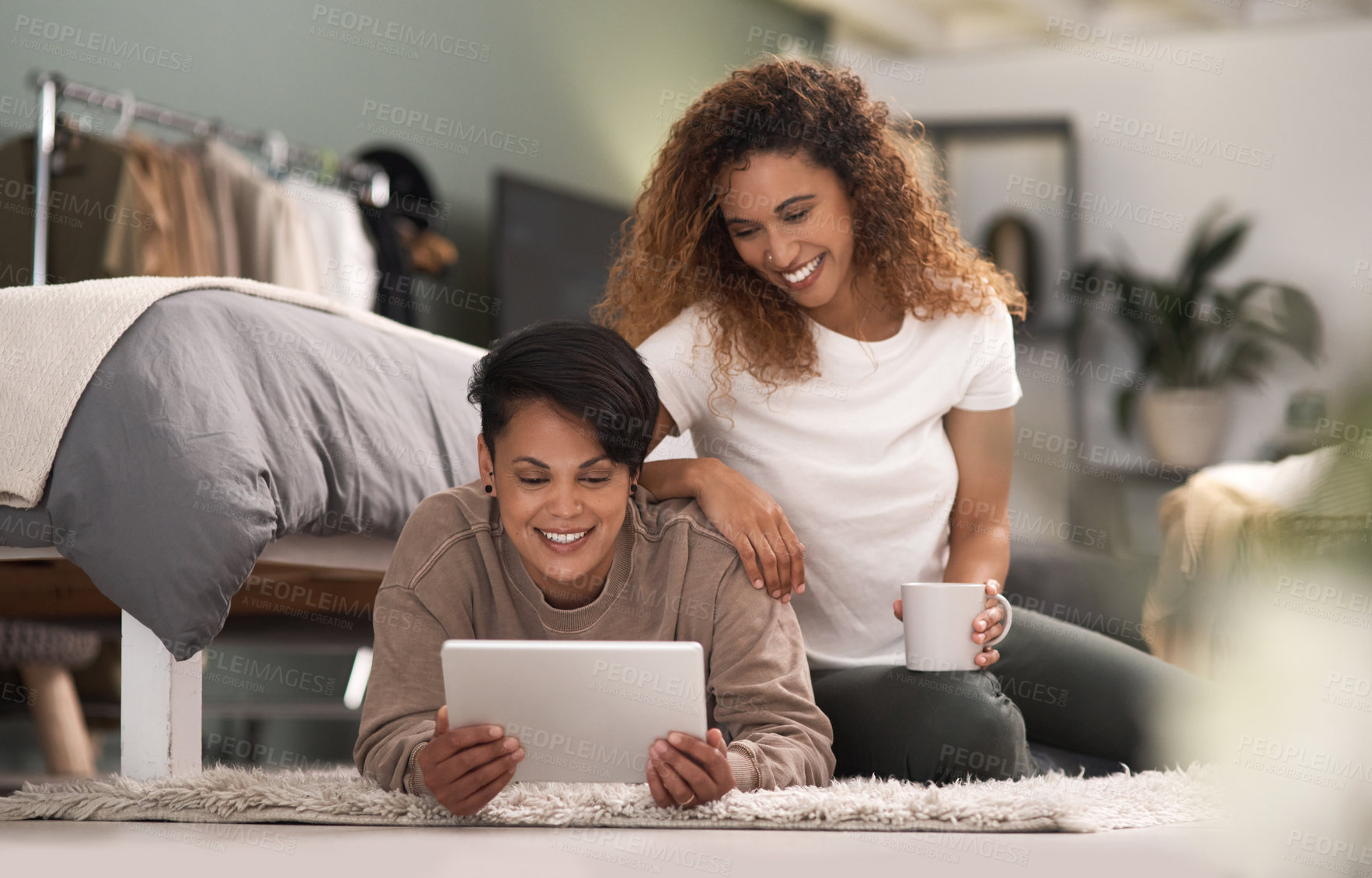 Buy stock photo Shot of a young lesbian couple using a tablet while relaxing in their bedroom