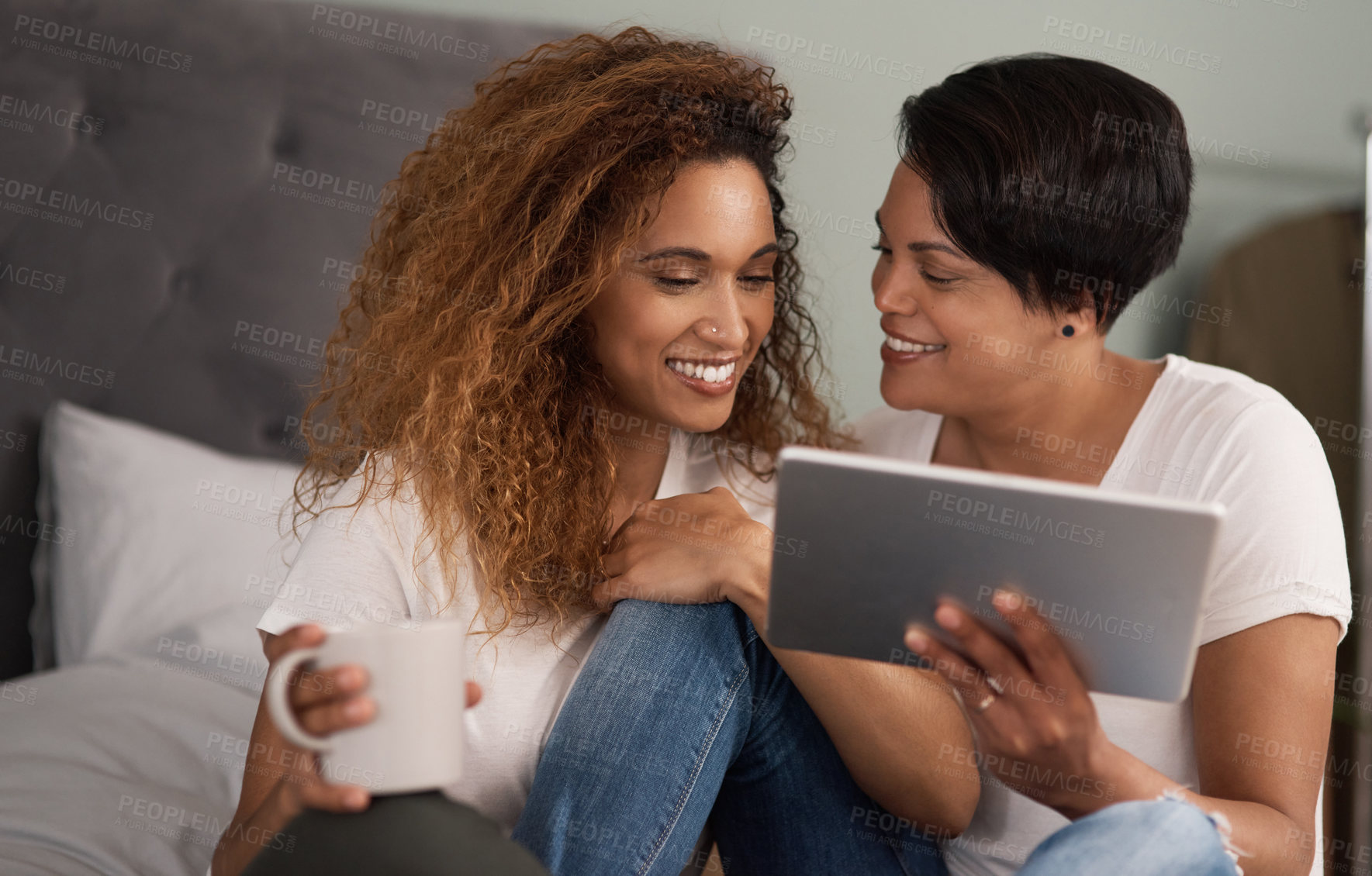 Buy stock photo Happy, women and lesbian couple in bedroom with tablet, watch movie and bonding together on weekend. Smile, lgbt people and relax in home with tech, tea and search website for streaming online film.