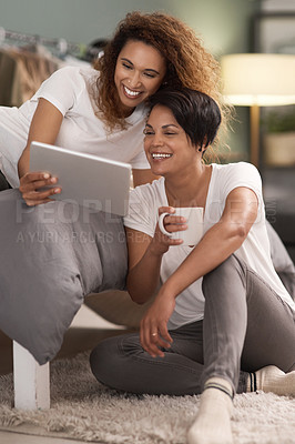 Buy stock photo Shot of a young lesbian couple using a tablet while relaxing in their bedroom