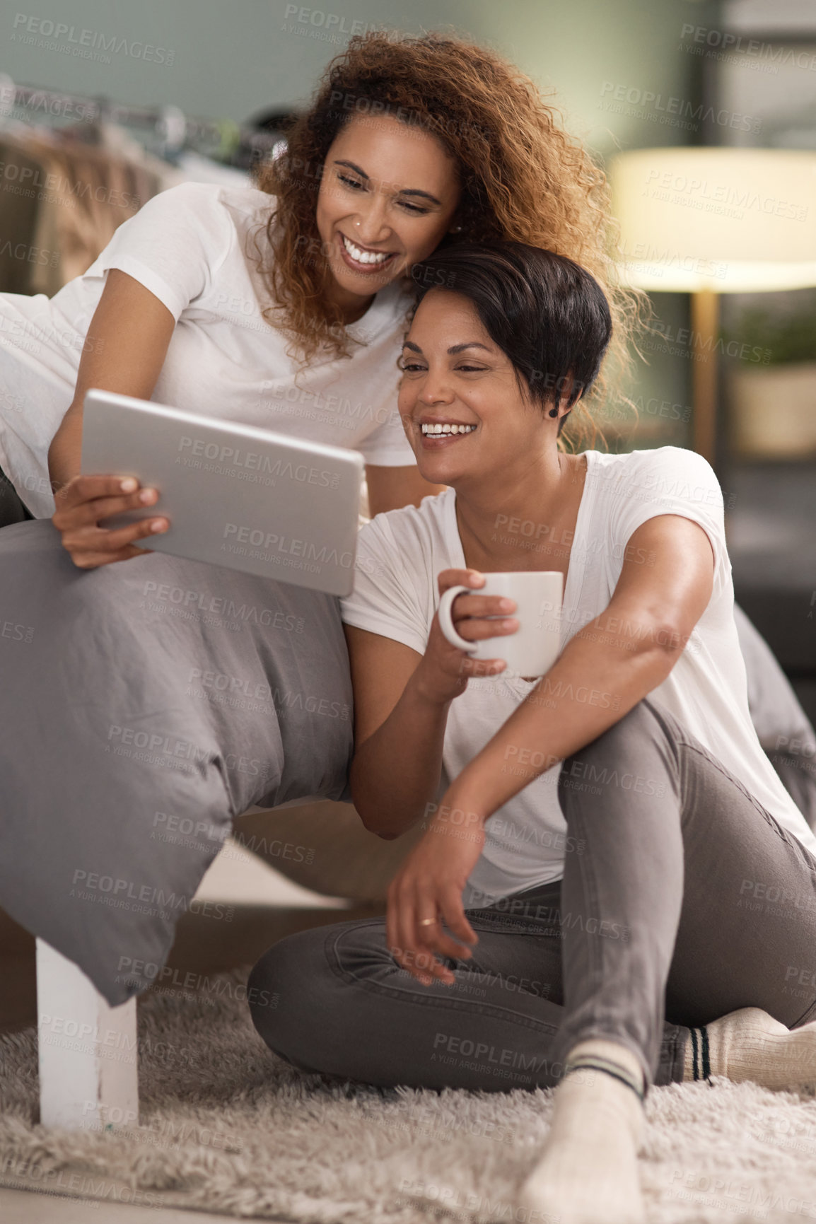 Buy stock photo Shot of a young lesbian couple using a tablet while relaxing in their bedroom