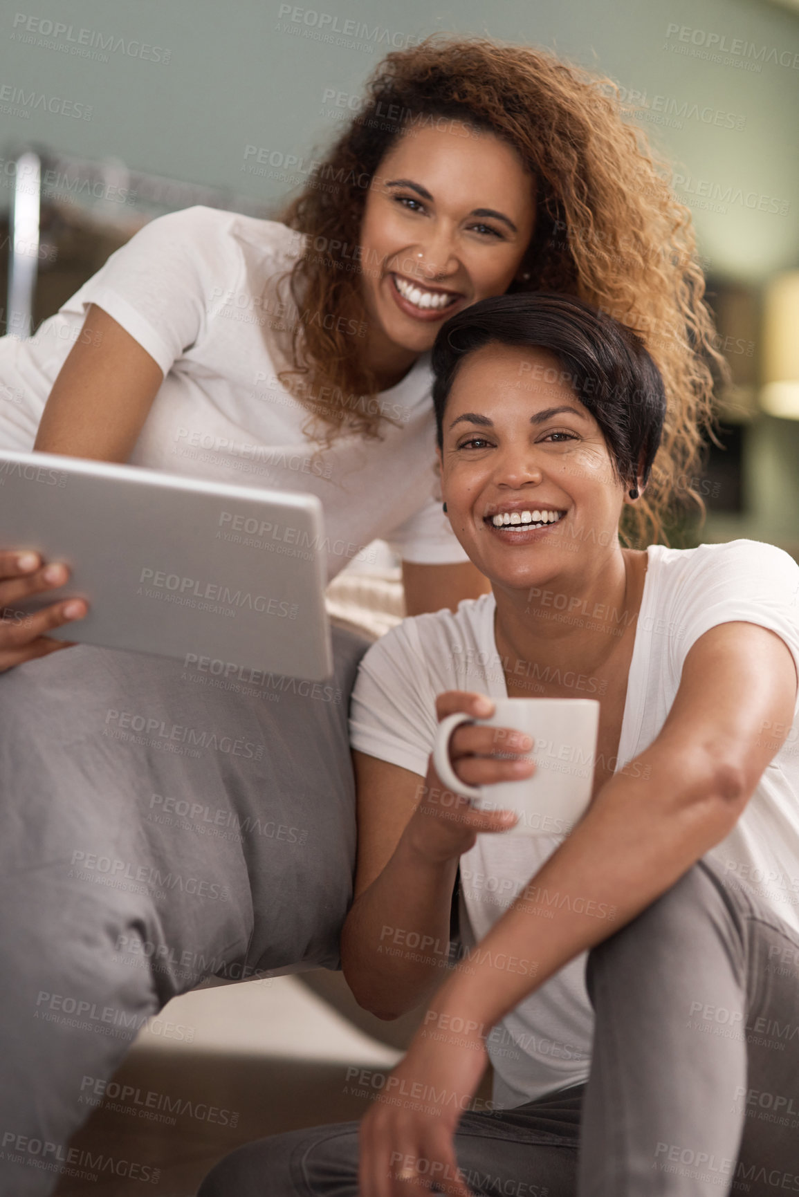 Buy stock photo Shot of a young lesbian couple using a tablet while relaxing in their bedroom