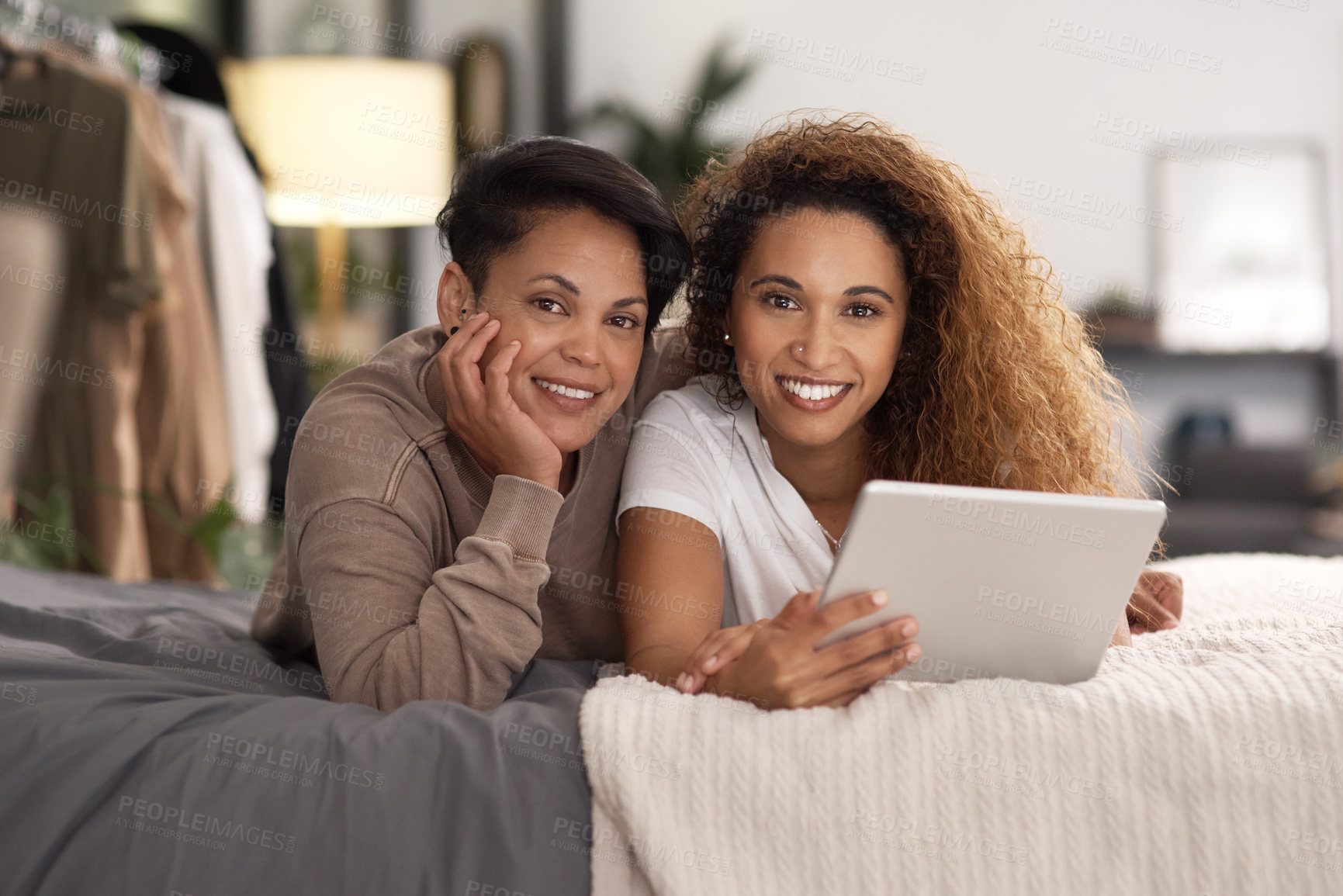 Buy stock photo Shot of a young lesbian couple using a tablet while relaxing in their bedroom