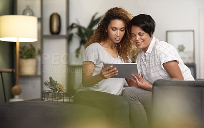 Buy stock photo Shot of a young lesbian couple using a tablet while relaxing in their lounge at home