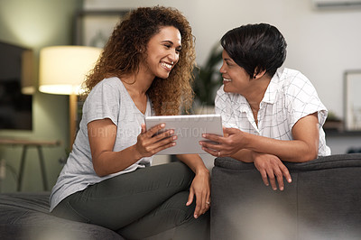 Buy stock photo Shot of a young lesbian couple using a tablet while relaxing in their lounge at home