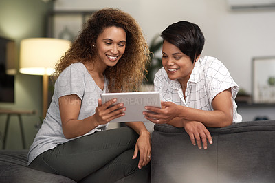 Buy stock photo Shot of a young lesbian couple using a tablet while relaxing in their lounge at home