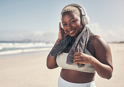 Buy stock photo Shot of a sporty young woman wearing headphones and a towel around her neck on the beach