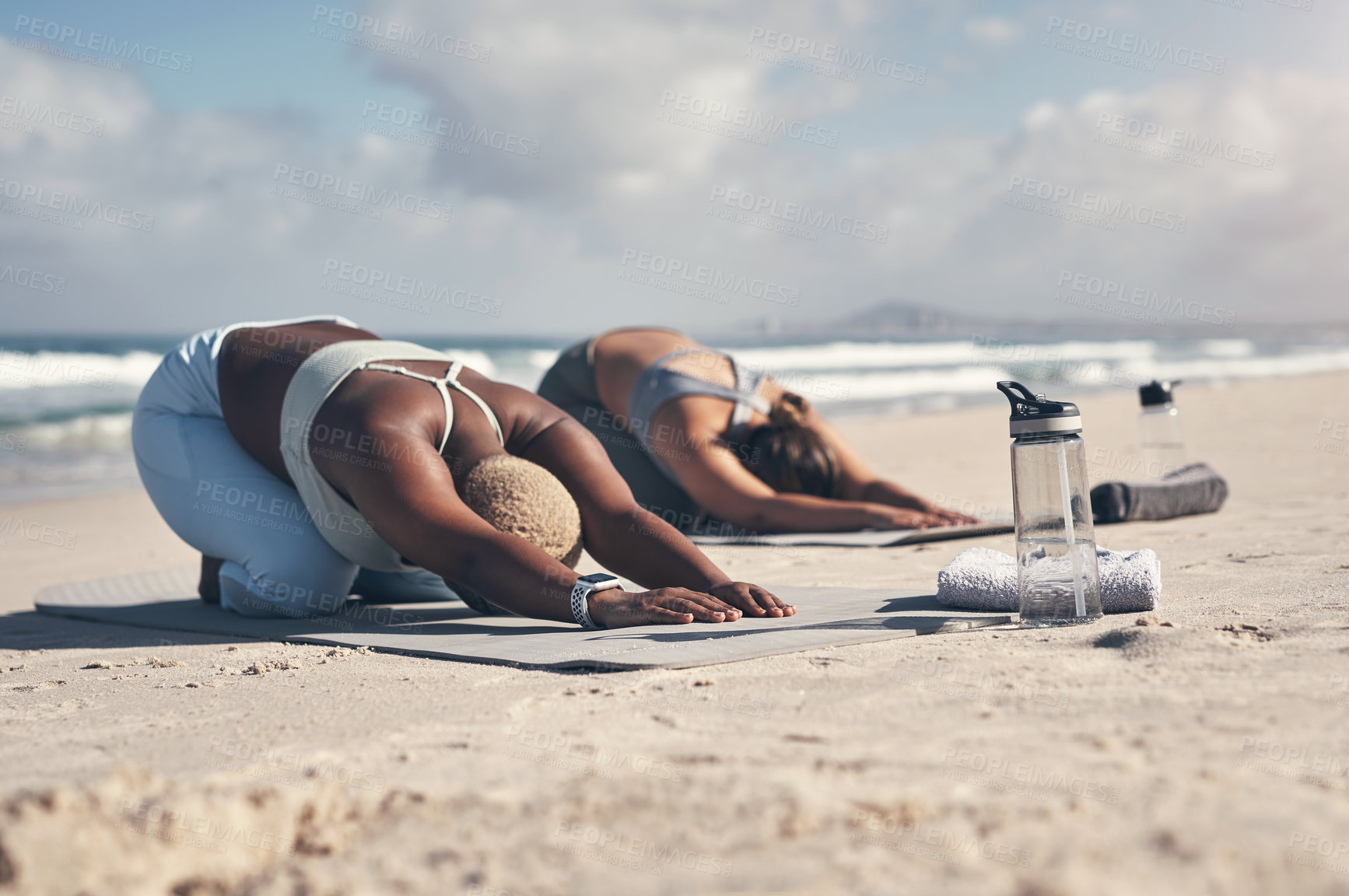 Buy stock photo Shot of two young women practicing yoga on the beach