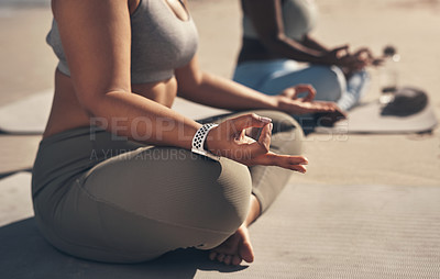 Buy stock photo Shot of two young women meditating during their yoga routine on the beach