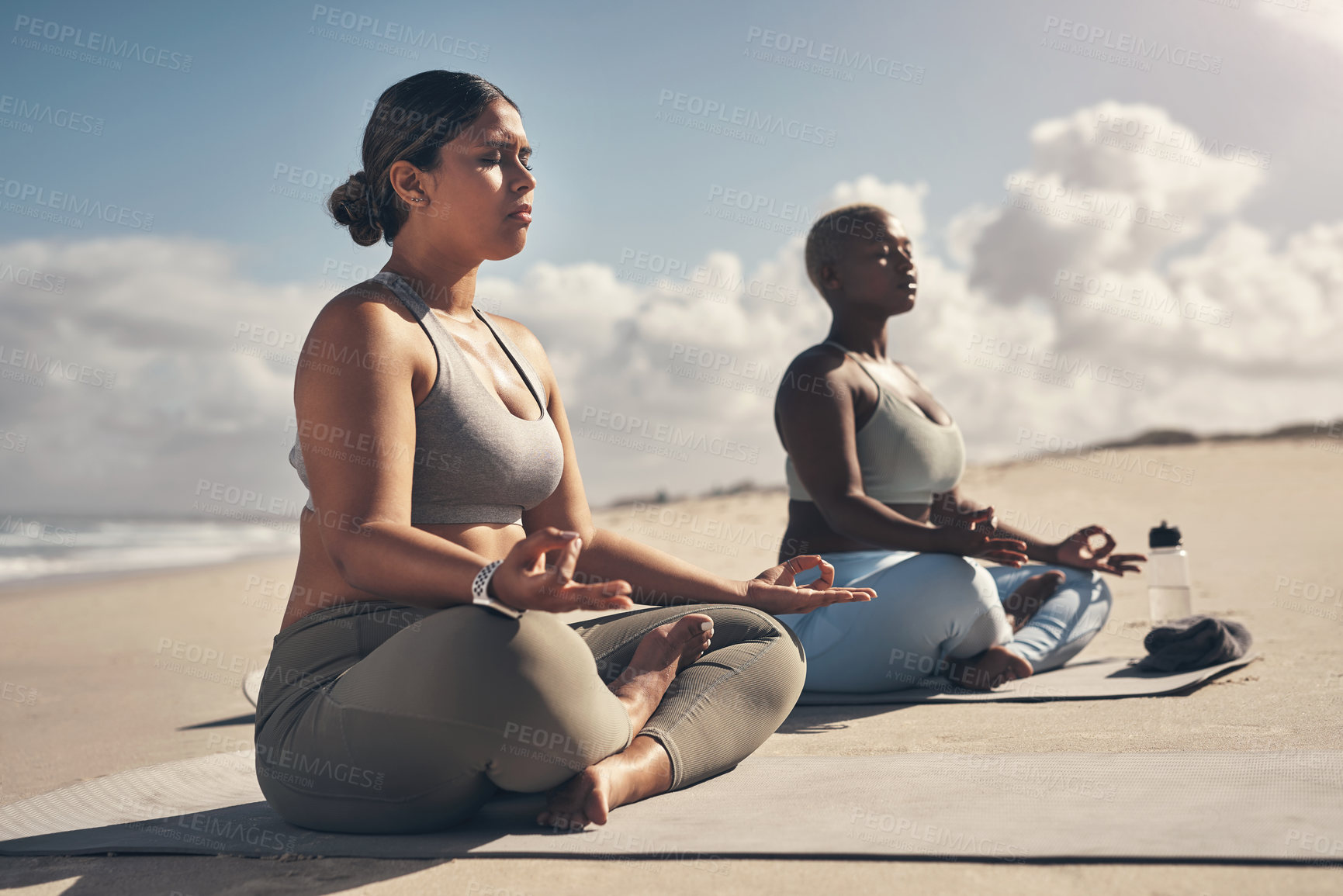 Buy stock photo Shot of two young women meditating during their yoga routine on the beach