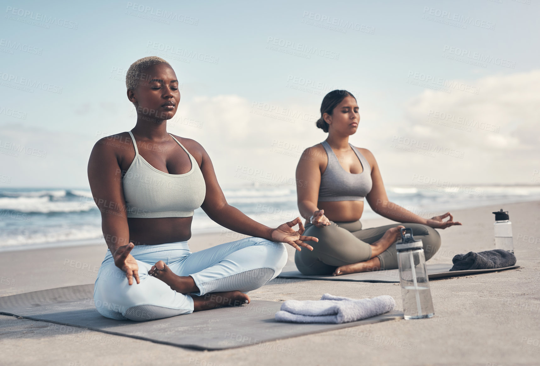 Buy stock photo Shot of two young women meditating during their yoga routine on the beach