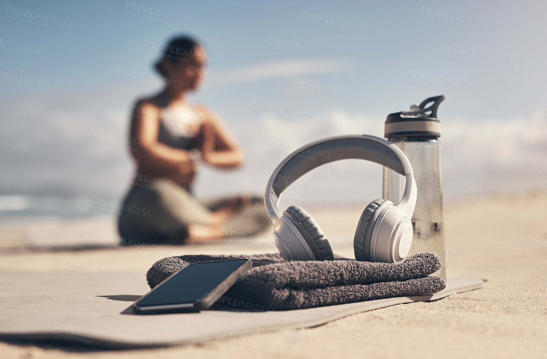 Buy stock photo Shot of a cellphone, headphones, towel and water bottle on the beach