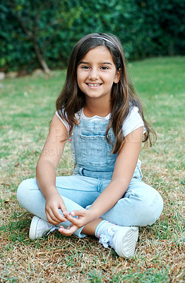 Buy stock photo Girl child, portrait and happy or cross legged in nature, innocent and sitting on grass in backyard lawn. Kid, smile and sweet for playful childhood, bright and cute for summer in garden or park