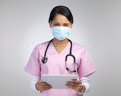 Buy stock photo Cropped portrait of an attractive young female healthcare worker wearing a mask and stethoscope while using her tablet in studio against a grey background