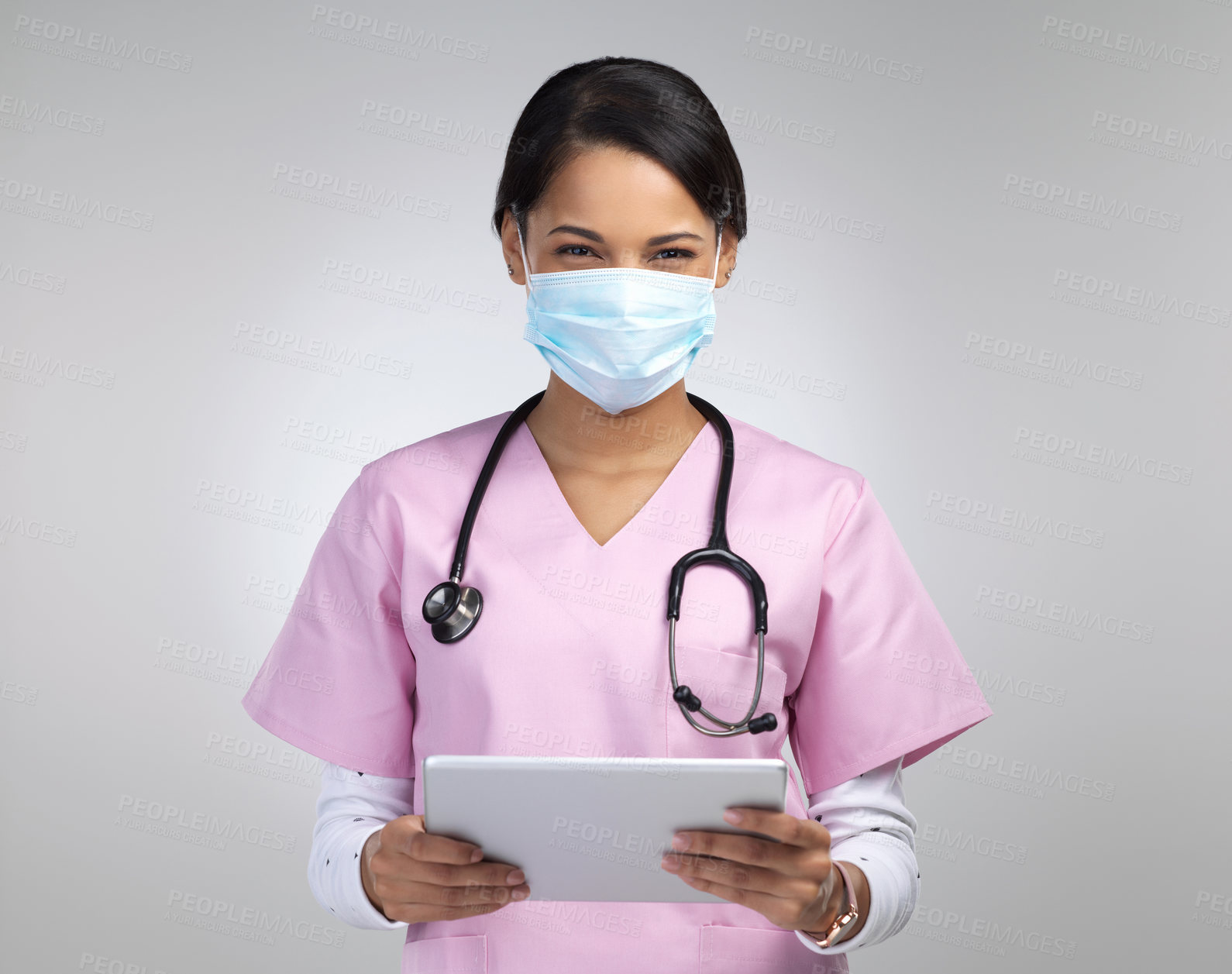 Buy stock photo Cropped portrait of an attractive young female healthcare worker wearing a mask and stethoscope while using her tablet in studio against a grey background