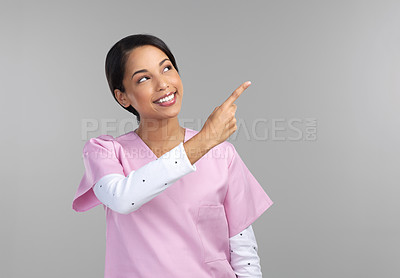 Buy stock photo Cropped shot of an attractive young female healthcare worker pointing towards copyspace in studio against a grey background