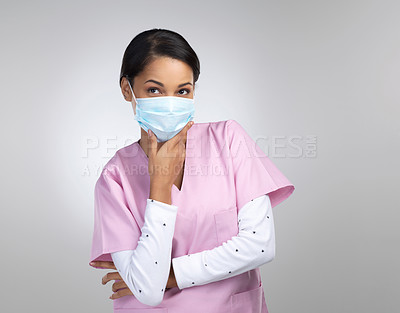 Buy stock photo Cropped shot of an attractive young female healthcare worker wearing a mask and looking thoughtful in studio against a grey background