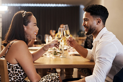Buy stock photo Shot of a happy young couple sitting together and toasting with champagne during a New Year's dinner party
